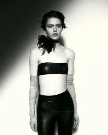 Monochrome studio portrait of a young adult woman in a bandeau top and leggings with feather accessory, posing against a backdrop.