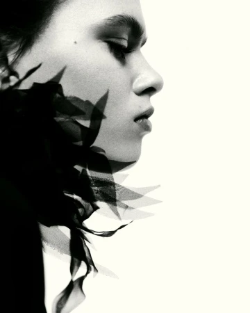 Black and white profile portrait of a model with sheer fabric shadows along her jawline against a stark white backdrop.