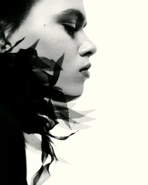 Black and white profile portrait of a model with sheer fabric shadows along her jawline against a stark white backdrop.