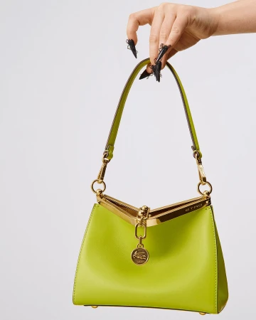 A hand with pointed black nail art holds a lime green leather Etro Mini Vela bag with gold hardware on a white background.