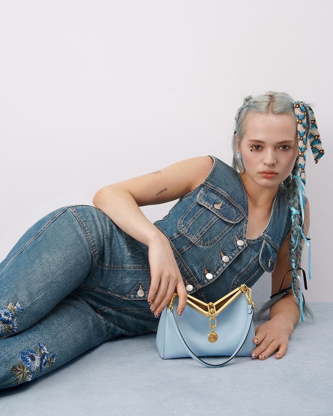 Portrait of a woman in denim posing with a blue purse in front of a white background, showcasing fashion and style in a studio setting.
