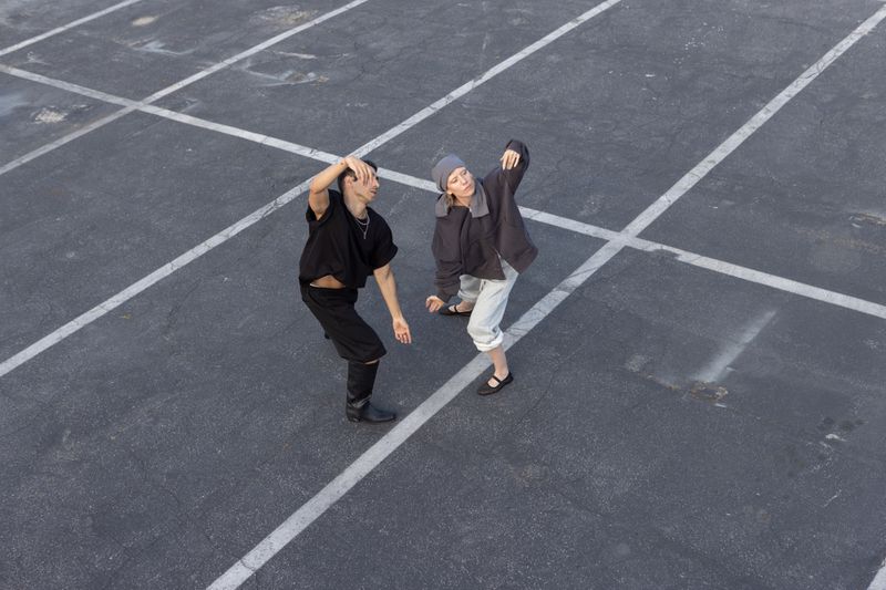 Two people dance in an urban outdoor space; concrete ground with white lines forms a minimalist stage for this dynamic performance.