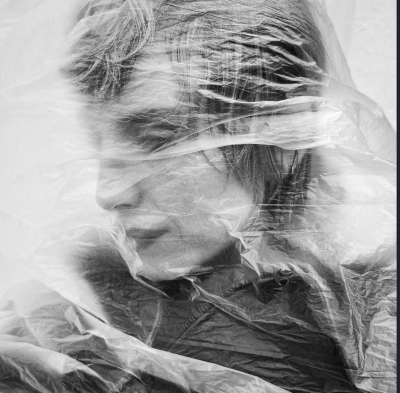 Monochrome portrait of an adult woman seen through clear plastic, creating a textured and obscured artistic effect in the studio.