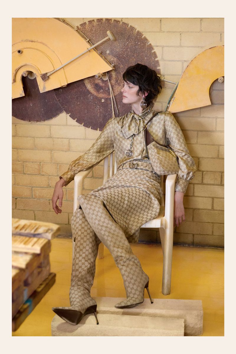 Fashion photo featuring a woman in a patterned skirt and blouse with matching thigh-high boots, posing on a chair in studio setting.