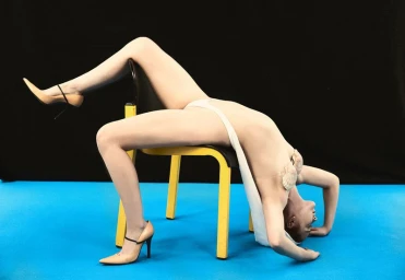 Model draped backwards over a yellow chair wearing beige high heels against a black and blue background for Neo 2.