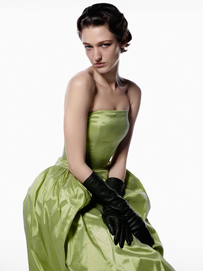 Elegant woman in a green strapless dress and black gloves poses against a white background, showcasing a timeless and sophisticated fashion aesthetic.