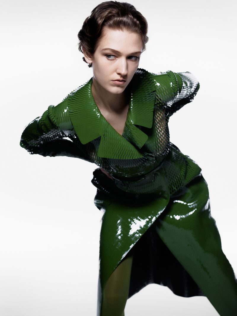 Fashion portrait of a woman in a green shiny outfit, posed against a white backdrop, showcasing a modern and stylish look.