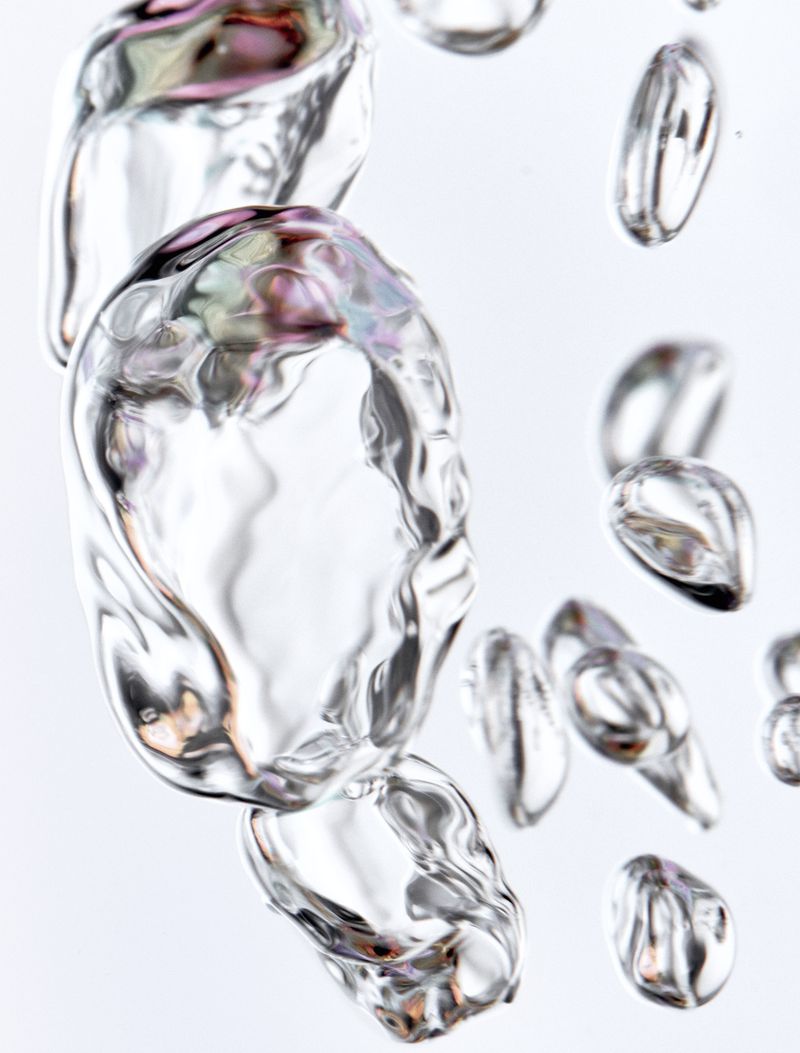 Macro shot of clear, iridescent water bubbles against a bright white background with smooth surfaces and organic liquid forms.