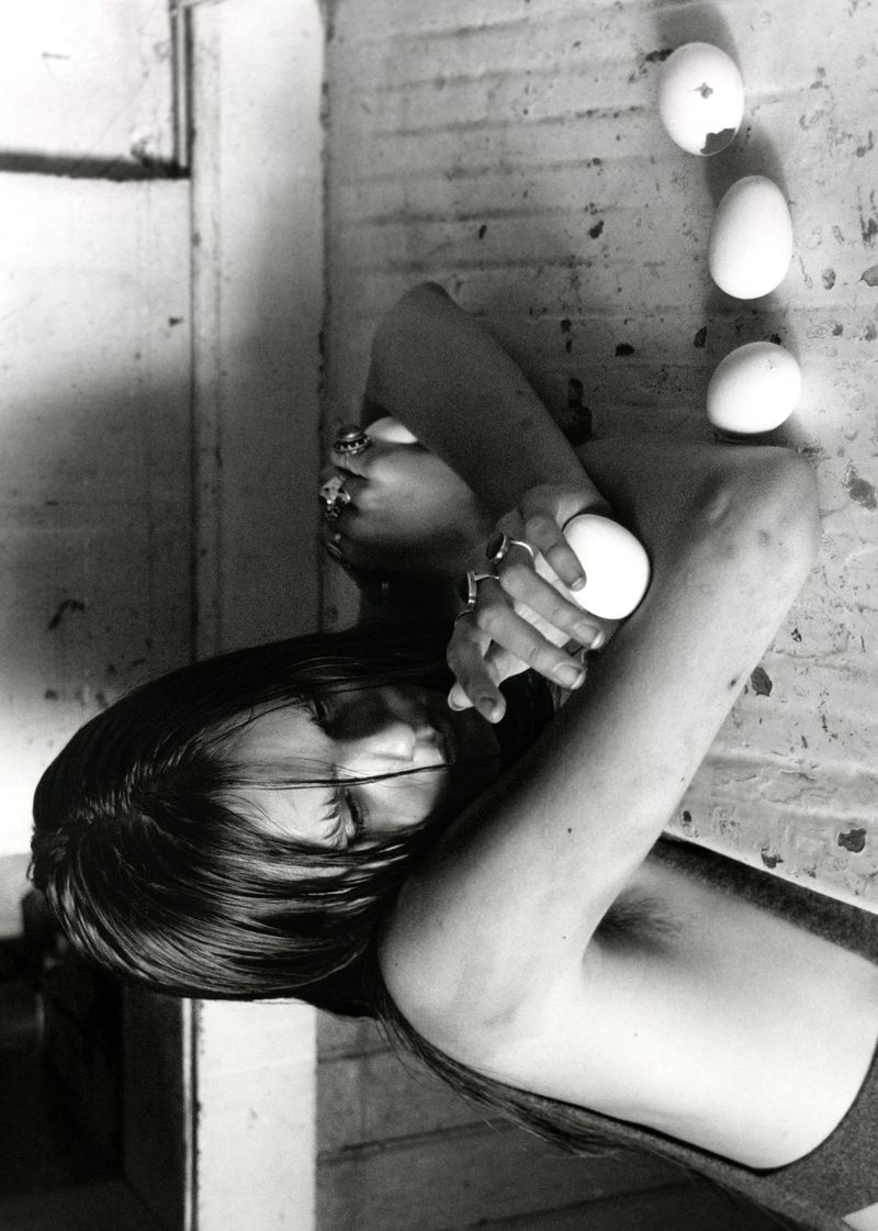 Monochrome artistic shot of a reclining shirtless person holding an egg, with a row of eggs positioned in the background.