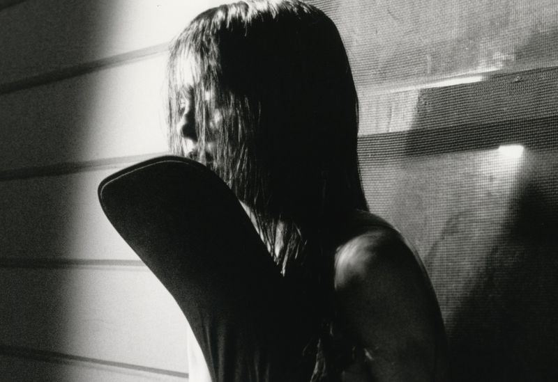 Monochrome portrait of a woman with long dark hair posing indoors in front of a textured background with light and shadow play.