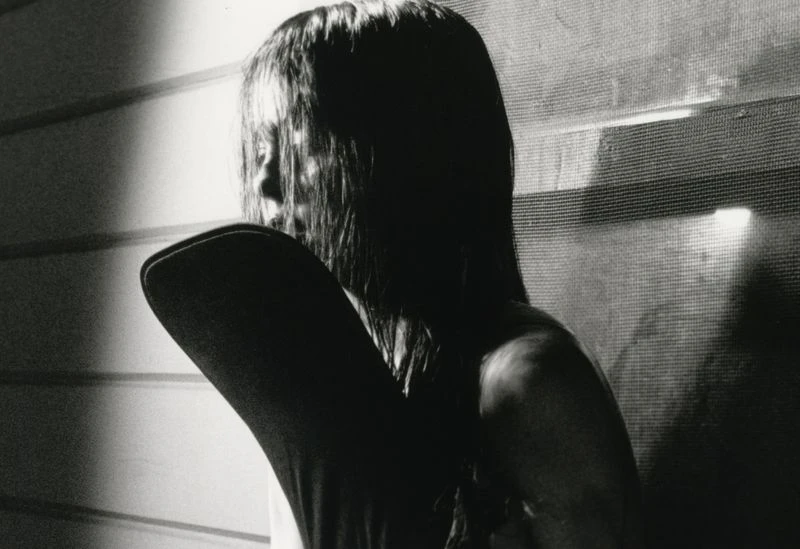 Monochrome portrait of a woman with long dark hair posing indoors in front of a textured background with light and shadow play.