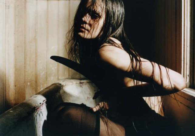 Dramatic photograph of a wet-haired, partially undressed adult female in a bathtub, emphasizing dark, moody lighting and a gritty aesthetic.