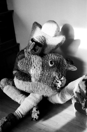 Black and white photo of two knitted animal dolls, one a sheep, on a wooden floor with sunlight casting shadows on the wall.