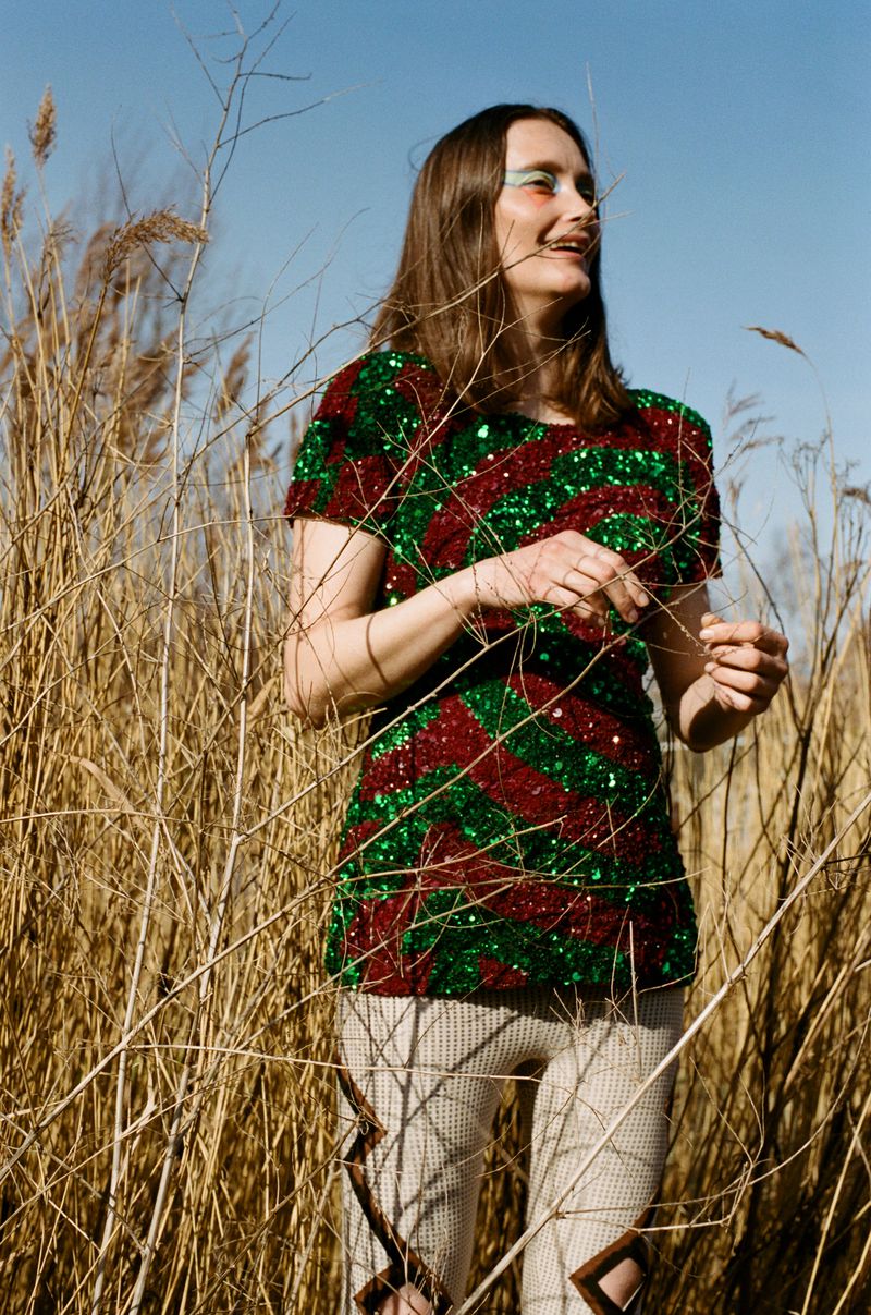 Woman in a sequin shirt standing in a field of tall grasses with a blue sky. Fashion outdoor shot with natural light.