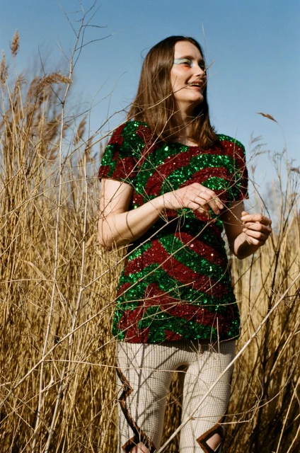 Woman in a sequin shirt standing in a field of tall grasses with a blue sky.  Fashion outdoor shot with natural light.