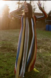 Model Iekeliene Stange poses in a multi-colored vertically striped maxi dress with raised painted palms in a grassy field.