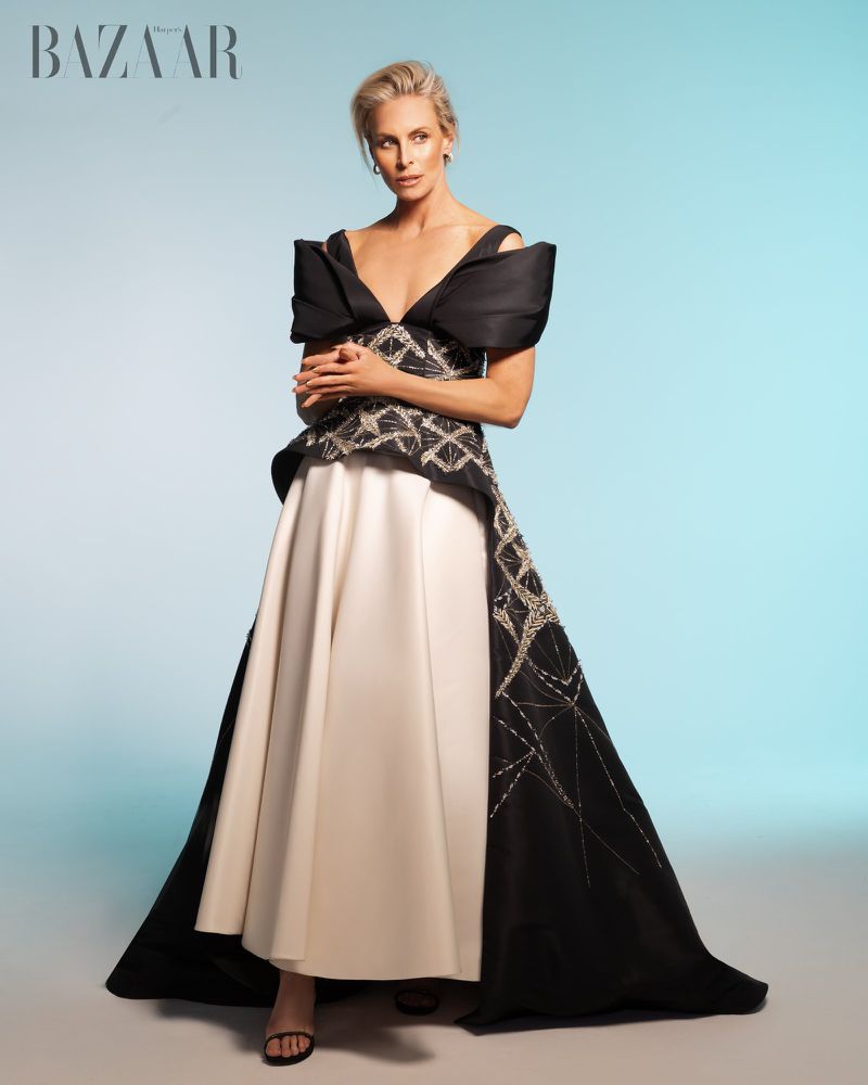 Elegant woman in a black and white gown poses in a studio. The dress features ornate details and a dramatic silhouette.