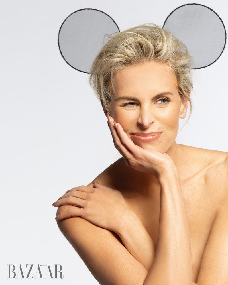 Adult woman with bare shoulders posing in a photo studio with 'mouse ears' accessory on a white backdrop, shot in portrait orientation.