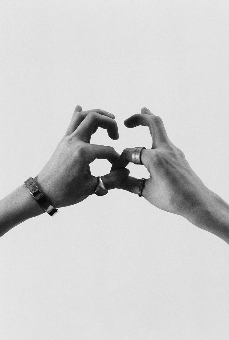 Two hands create an abstract shape against a white background in a black and white photograph. Silver rings and bracelets are visible.