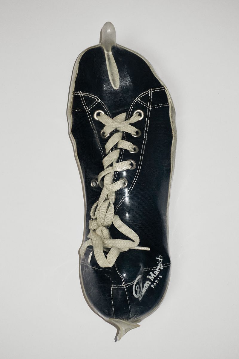 Elevated shot of a glossy black shoe-shaped object with white laces and a small heel-like point at the toe on a white surface.