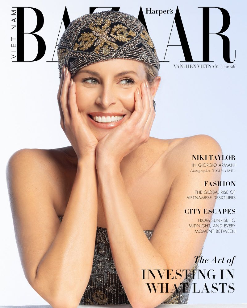 Magazine cover featuring a smiling blonde woman wearing a beaded cap, resting her face in her hands, shot against a light blue backdrop.
