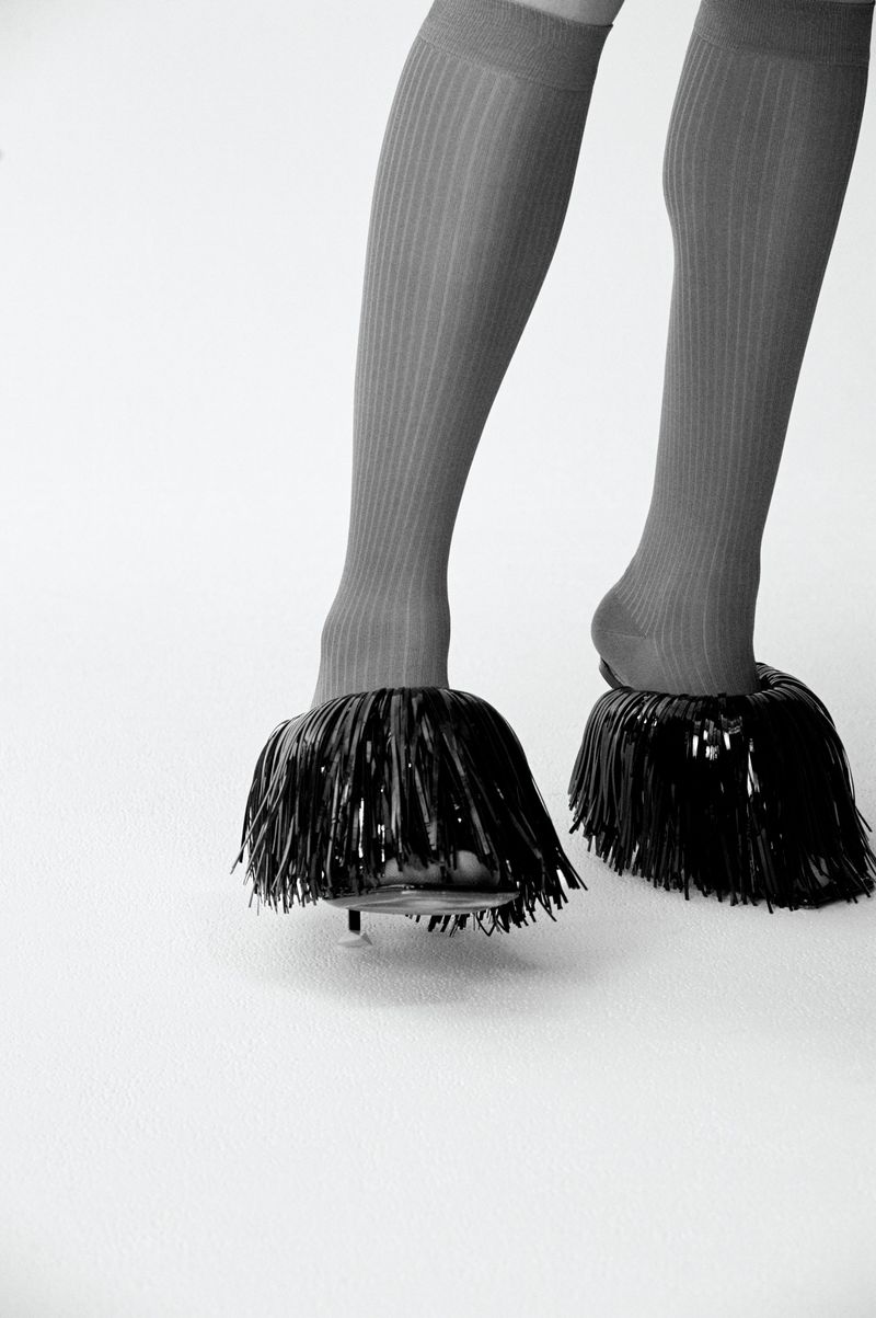 Legs of a person wearing gray ribbed socks and black shoes with fringe, on a white background. Fashion footwear studio shot.