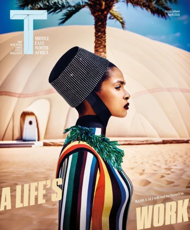 Ramla Ali wearing a striped top, beaded collar, and black pillbox hat in front of a desert dome building.