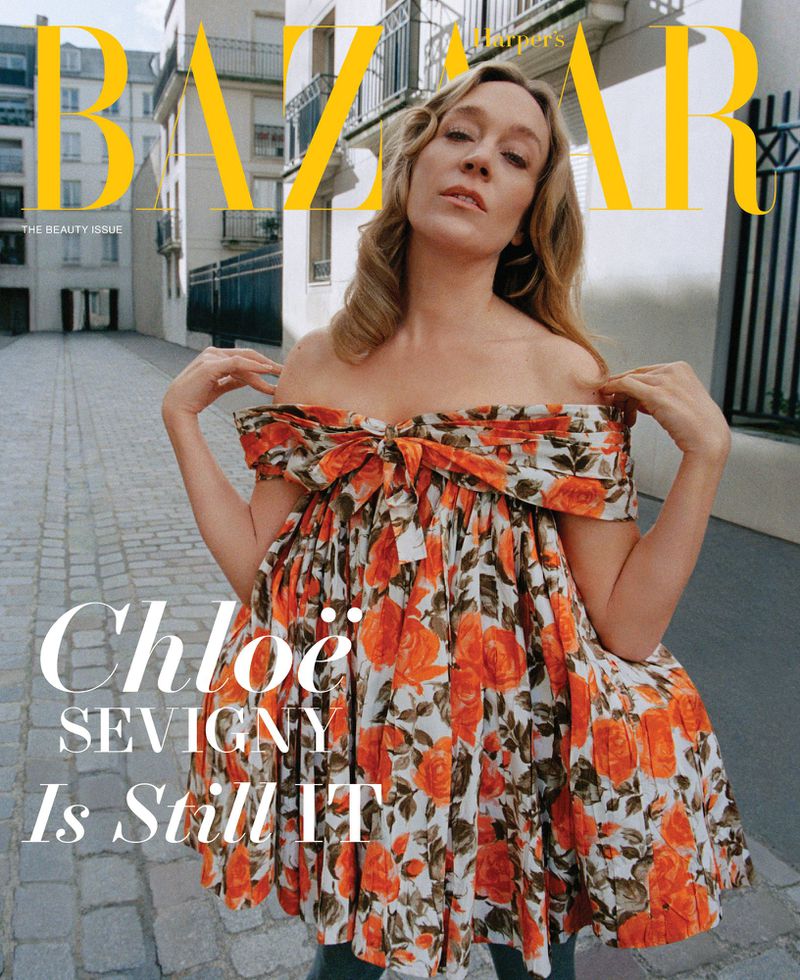 Chloe Sevigny on a magazine cover wearing a floral print dress, outside on a cobblestone street with stone buildings in the background.