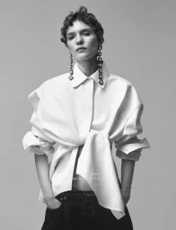 Penelope Ternes wearing an oversized tied white shirt and dangling geometric earrings against a studio backdrop.