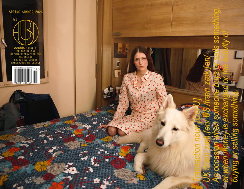 Woman in patterned pajamas sits with a white dog on a floral bed in an indoor setting, next to magazine text overlay and furniture.