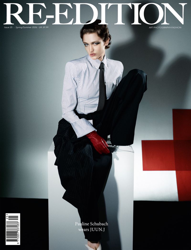 Magazine cover featuring a posed female model wearing a striped shirt, dark tie, black pants, and red gloves, against a grey studio backdrop.