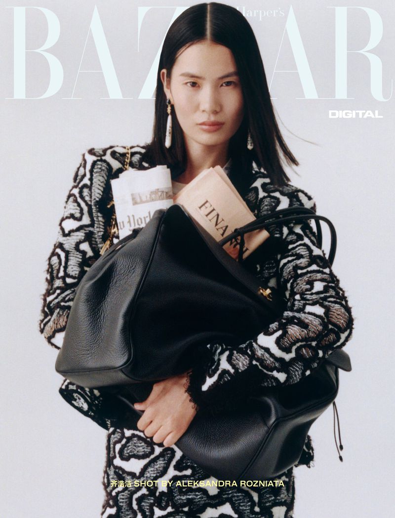 Fashion editorial cover of Asian woman holding black leather bag and wearing black and white print suit against white backdrop.