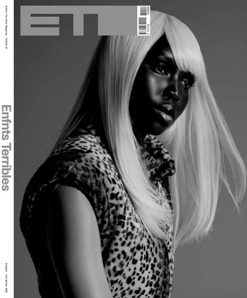 Monochrome close-up of a stylish dark-skinned adult female wearing a blonde wig and leopard print top against a grey background.