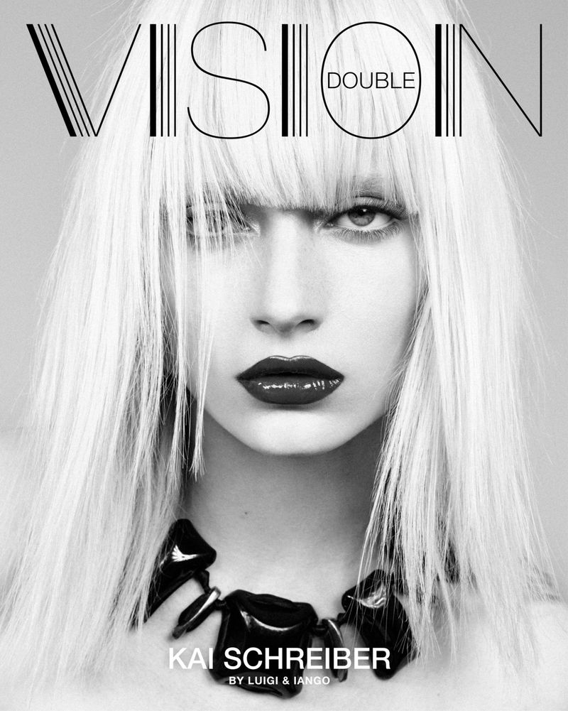 Black and white portrait of a young woman with long blonde hair, dark lipstick, and a black necklace, as seen on a magazine cover.