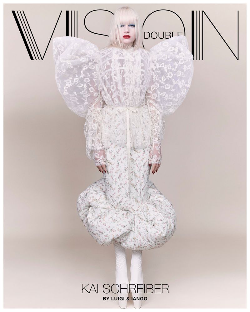 A fashion magazine cover features Kai Schreiber wearing a large white floral dress and striking makeup, centered against a tan backdrop.