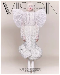 Kai Schreiber wearing a sculptural white floral lace gown with exaggerated puff sleeves against a pale studio background.