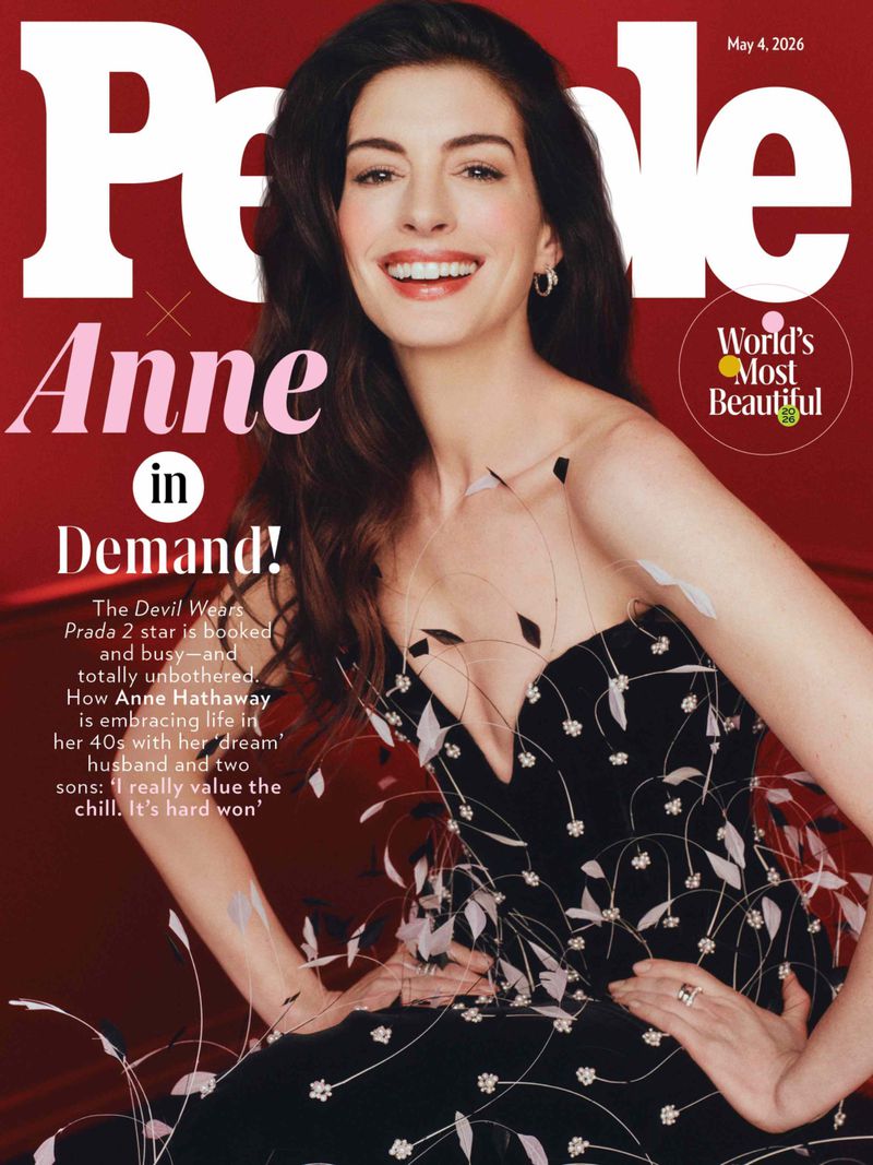 Anne Hathaway graces the cover of People magazine, May 4, 2026 issue, wearing a black dress with white floral accents, set against a red backdrop.