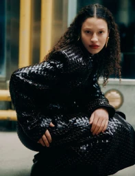 Model Elsa Vouga crouching in a textured black woven coat with gold earrings for Elle Mexico.