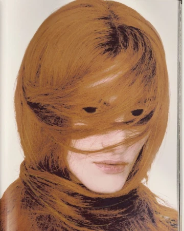 Fashion portrait of a model with copper-colored hair partially obscuring her face, shot in a photo studio with a white background.