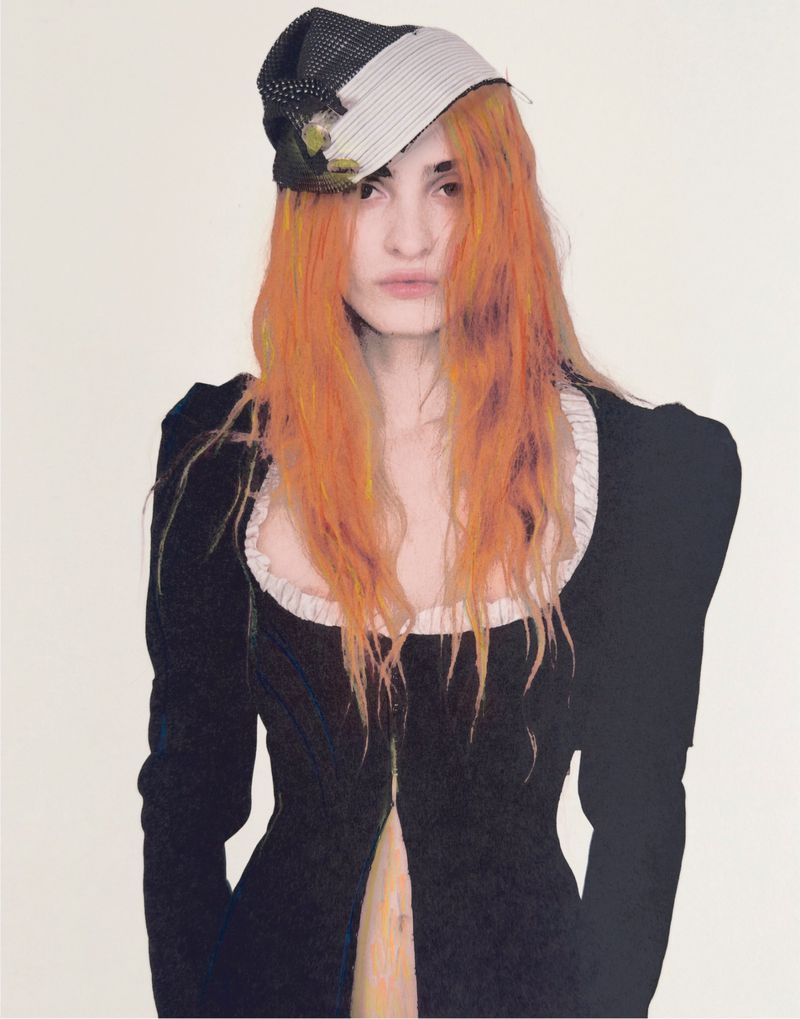 Portrait of a woman with orange hair wearing a black dress with a white collar and a patterned hat against a white background.