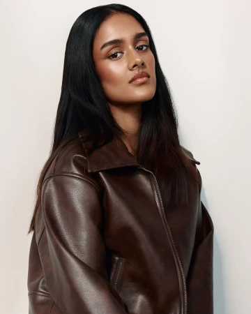 Portrait of a woman with long dark hair wearing a brown leather jacket against a white background in a studio setting.