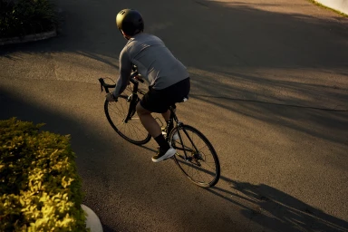 Cyclist in a helmet and grey jersey riding a road bicycle on asphalt pavement during late afternoon sunlight.