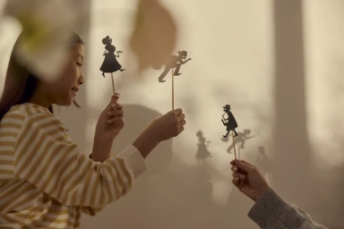 A young girl and another person holding up paper shadow puppets against a sunlit wall for Melrose Park by Sekisui House