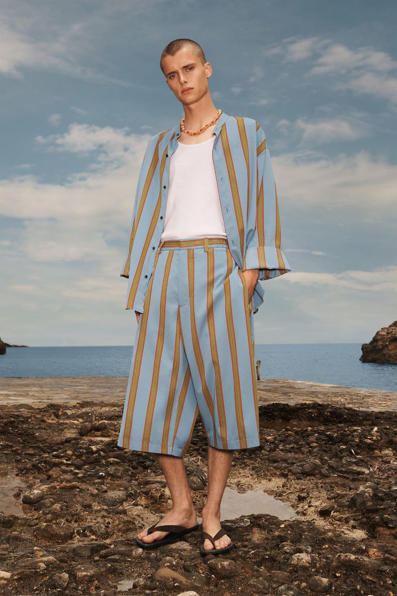 Model standing on a rocky shore wearing a blue striped matching shirt and shorts set over a white tank top