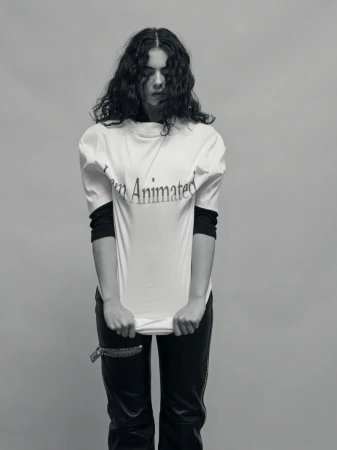 Monochrome portrait of a young woman with curly hair wearing a 'I am Animated' t-shirt and holding up the bottom of the shirt.