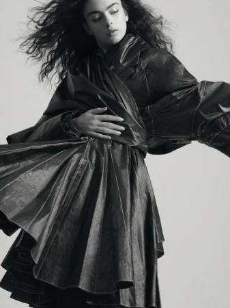 Monochrome portrait of a young woman in a dark, flowing dress, with expressive, voluminous hair, and soft, diffused lighting in studio.