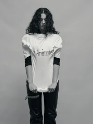 Deva Cassel in an oversized white graphic tee and black leather trousers against a grey seamless studio backdrop.