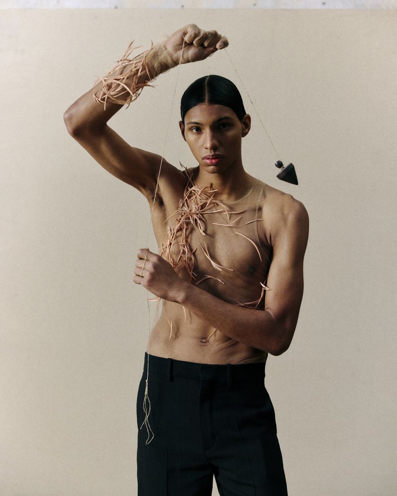 Person with twigs art. Close-up studio shot of a slender adult with bare torso, black pants, and dark hair with twigs as art.