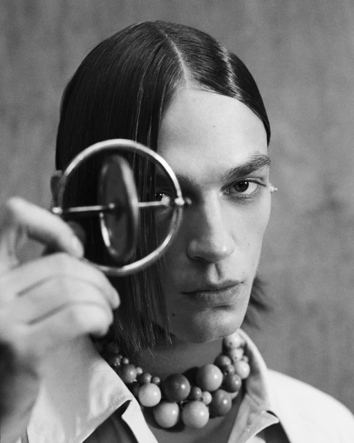 Black and white portrait of an adult male with long hair, wearing a bead necklace, and holding a round object in his hand.