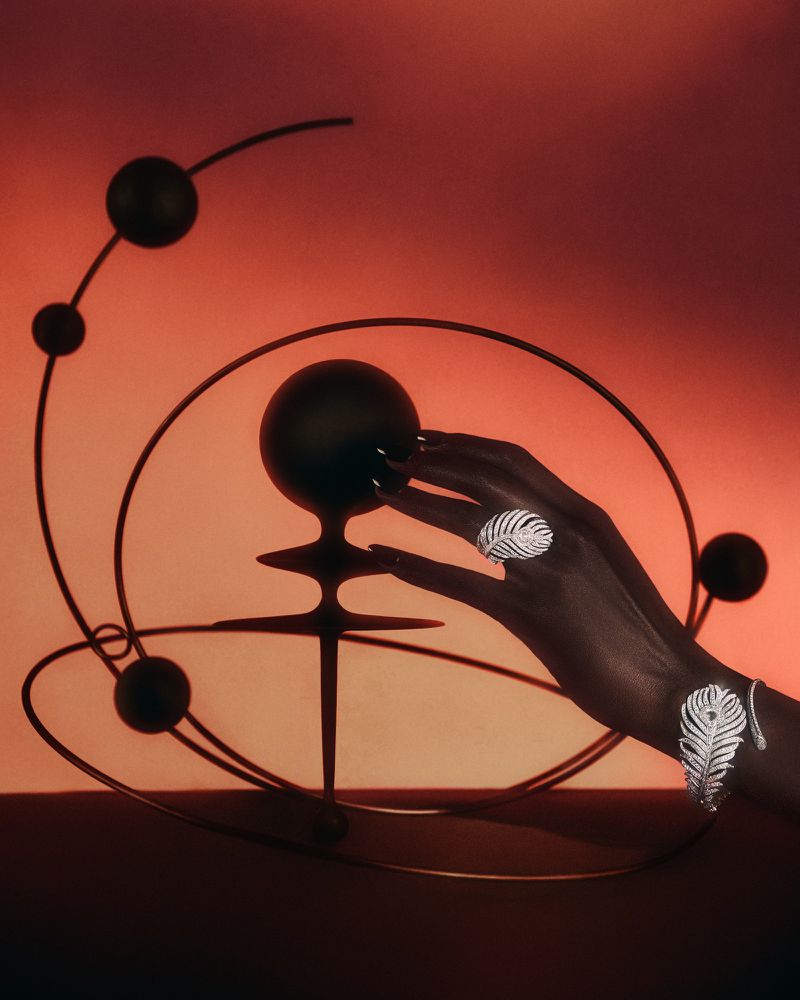 Close-up of a Black woman's hand adorned with jewelry, gracefully posed near an abstract metal sculpture with warm, gradient lighting.
